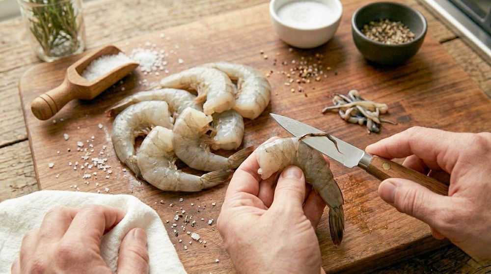 Raw shrimp being deveined before cooking showing proper prep technique on a cutting board