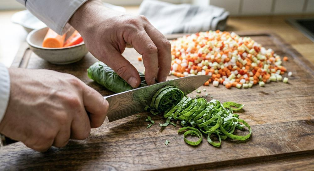 Chiffonade cut — rolled herbs being sliced into thin ribbons on a cutting board