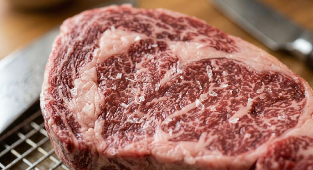 Close-up of a raw Wagyu ribeye steak showing extraordinary intramuscular fat marbling with flaky sea salt